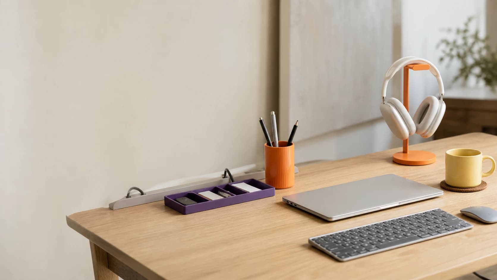 An organized minimalist desk setup with AM3D system in use — purple drawer organizer, orange pen cup, orange headphone stand with white headphones, yellow mug on blue coaster, MacBook and keyboard